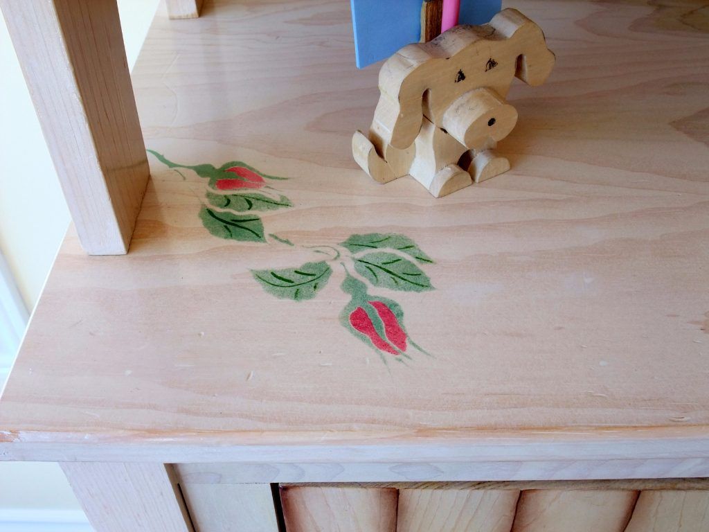 Folk art rose vines hand-painted on pale wood furniture, with a small carved dog